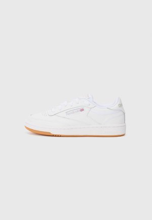 White Reebok low-top sneaker with gum sole, laces, and Reebok logo with British flag on side, shown from outer side on gray background.