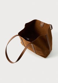 Pruun seemisnahast kandekott pruuni nahkkäepidemetega, avatud pealmise osaga ja nööpkinnitusega. Sisemus tundub mahukas ja voodrita.