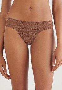 Bruine kanten thong met bloemmotieven en een geschulpte tailleband. Zachte textuur, minimalistische dekking en zichtbare naaddetails.