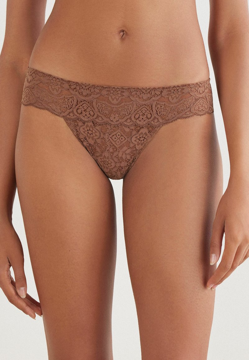 Bruine kanten thong met bloemmotieven en een geschulpte tailleband. Zachte textuur, minimalistische dekking en zichtbare naaddetails.