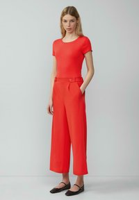 Rode gebreide top met korte mouwen, gecombineerd met hooggewaiste, losse rode broek met zijzakken en knoopaccenten, aangevuld met zwarte ballerina's.