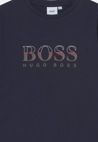 T-shirt in cotone blu navy con logo "BOSS HUGO BOSS" in bianco e grigio con linee di accento rosse, scollo rotondo e maniche corte.