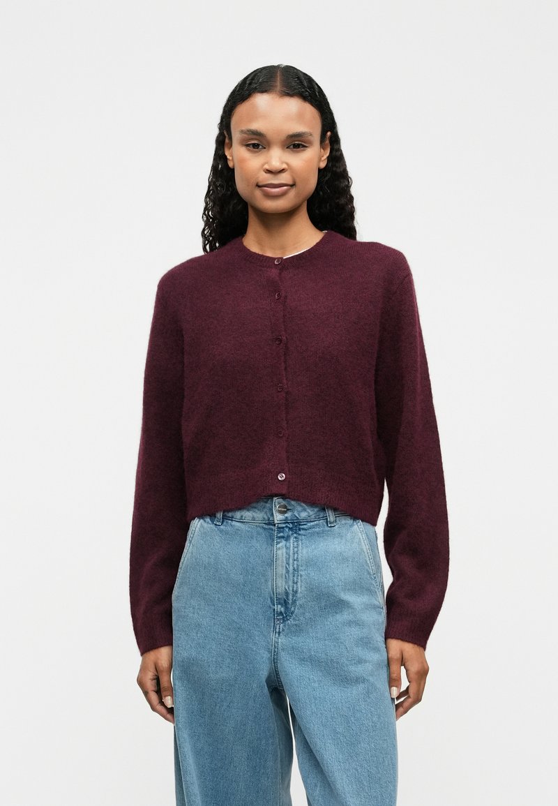 Burgundy knit cardigan with long sleeves, round neckline, and a button closure. Paired with high-waisted light blue denim jeans.