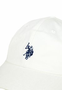 Bela bombažna kapa z vezenim logotipom polo igralca v mornarsko modri barvi. Gladek otip, ukrivljen ščitnik in zračne luknje za prezračevanje.