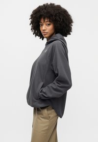 Γκρι φλις φούτερ με άνετη εφαρμογή, διαθέτει εμπρόσθια τσέπη και κουκούλα με ρυθμιζόμενο κορδόνι. Συνδυάζεται με μπεζ παντελόνι.