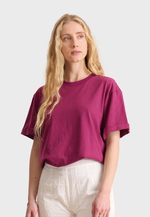 T-shirt en coton fuchsia avec des épaules tombantes, des poignets roulés et une coupe décontractée, associé à un pantalon blanc texturé taille haute.