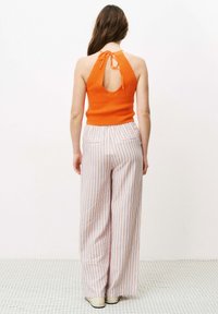 Oranje gebreide haltertop met een sleutelgatdetail op de rug, gecombineerd met wijde gestreepte broek in wit, roze en blauw, gemaakt van een lichte stof.