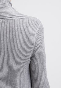 Maglione grigio a coste con colletto a scialle e una sottile texture, caratterizzato da righe verticali e una silhouette aderente.
