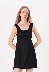 Vestido preto com decote quadrado, cintura ajustada e alças de ombro franzidas. Apresenta detalhes em ilhós e uma silhueta levemente evasê.