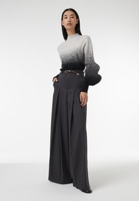 Hooghalzige, gradient gebreide trui die van lichtgrijs naar zwart overgaat, gecombineerd met hooggesneden, geplooide grijze broek en een riem.
