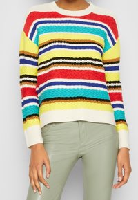 Monivärinen raidoitettu neulepusero, jossa on kirkkaanpunaisia, keltaisia, sinisiä ja vihreitä sävyjä, teksturoitu pinta ja ribbaatut hihansuut.