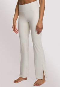 Crème kleurige flared broek met een hoge tailleband, voorzien van uitsparingen aan de zoom, gemaakt van soepel, rekbaar materiaal.