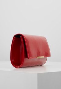 Borsa a mano rossa in pelle verniciata con un design strutturato, accessori in metallo dorato e chiusura a pattina. Texture liscia con una finitura lucida.
