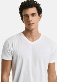 Hvid kortærmet T-shirt med V-hals, der har et diskret logo på brystet. Blødt stof med en glat overflade og et rent design.