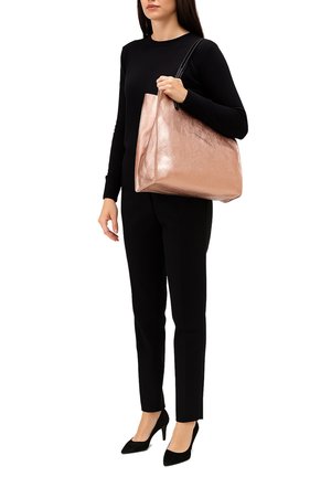 Borsa tote metallizzata color oro rosa con un design elegante, texture liscia e manici neri, tenuta da una persona in un completo nero.
