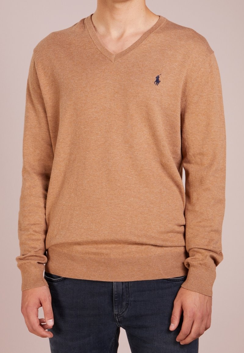 Pull à col en V, manches longues, couleur beige, texture tricotée avec poignets et ourlet côtelés. Présente un petit logo bleu marine sur le côté gauche de la poitrine.