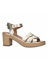 Metallic gouden sandalen met hakken en een stevige blokhak, met kruislings verstrengelde banden en decoratieve studs langs de basis. Verstelbare enkelband.