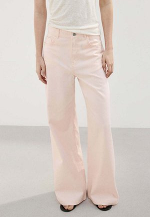 Pantalon large rose clair porté avec un haut blanc rentré et des sandales noires à bout ouvert, présenté sur une personne debout.