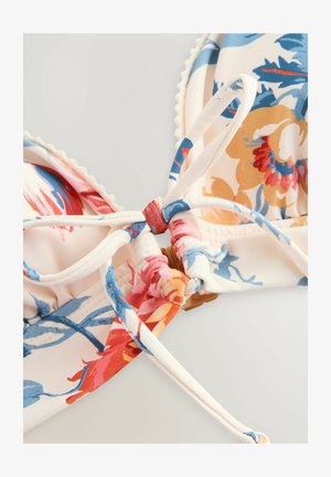 Cvetni bikini top z smetana osnovo, ki vsebuje rdeče, oranžne in modre vzorce. Zavezuje se na sredini z teksturirano obdelavo in valovitimi robovi.