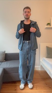 Blue fleece zip-up jacket over a black shirt, paired with light blue wide-leg jeans and white sneakers with gray accents. Wood floor background.