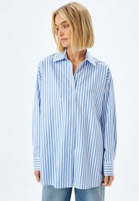 Blue and white striped oversized shirt, made of lightweight fabric, featuring a button-down front and wide cuffs.