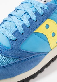 Blue suede and mesh sneaker featuring yellow accents, textured paneling, and flat laces. Durable rubber outsole with textured tread pattern.