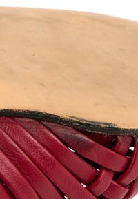 Gros plan de lanières en cuir rouge tissé sous un cuir marron clair lisse avec un bord noir légèrement usé.