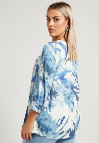 Blus med blommönster i blå nyanser, avslappnad passform, 3/4-ärmar och rund halsringning, tillverkad av ett lätt material.
