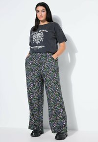 Zwarte graphic t-shirt met witte tekst en bloemenontwerp, gecombineerd met wijde broek met een veelkleurig bloemenpatroon en textuurstof.