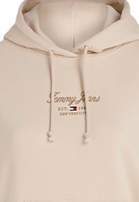 Felpa beige realizzata in morbido tessuto, con cappuccio regolabile tramite cordino, logo ricamato "Tommy Jeans" e tasca a marsupio.