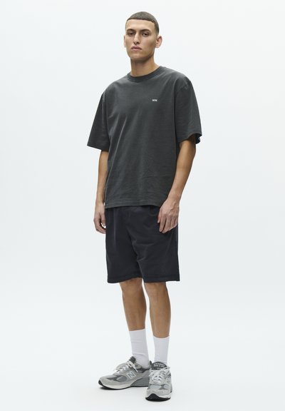 Mørkegrå bomulls-t-skjorte med korte ermer, kombinert med svarte shorts. Modellen har på seg hvite sokker og grå joggesko med reflekterende detaljer.