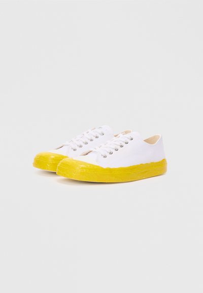 White canvas sneakers with a textured yellow rubber sole and metallic eyelets for laces. Rounded toe and minimal design.