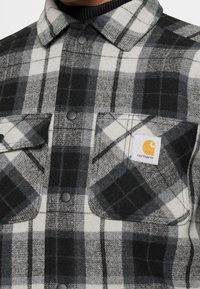 Schwarz-weiße karierte Flanellhemden mit Druckknöpfen, zwei Vordertaschen und einem Carhartt-Logopatch auf der linken Brust. Weicher Stoff.