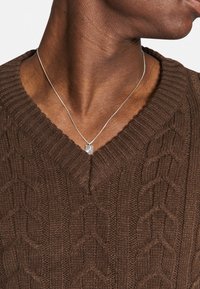 Collier chaîne en argent avec un pendentif carré, porté sur un pull marron texturé à col en V avec un motif en maille torsadée.