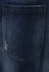 Mörkblå denimtyg med en enda bakficka. Strukturerad yta med synlig sömnad i en kontrasterande brun färg och lätt slitage.