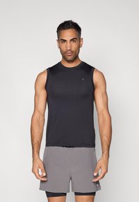 Fekete ujjatlan atlétatrikó sima anyagból, világosszürke rövidnadrággal párosítva. Egyszerű kerek nyakkivágással és minimális márkajelzéssel rendelkezik.