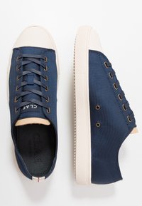 Baskets en toile bleu marine avec semelles en caoutchouc beige, dotées d'un bout rond, de détails œillets et de lacets. Tissu texturé et logo subtil visibles.