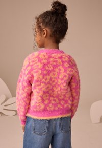 Blød lyserød sweater med gul leopardprint, rund halsudskæring og ribbede ærmekanter. Kombineret med højttaljede blå denimjeans.