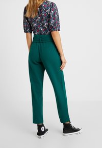 Turkusowe, dopasowane spodnie o gładkiej fakturze i wysokim stanie. W połączeniu z czarnymi trampkami za kostkę z białym logo gwiazdki.