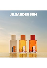 Tre Jil Sander Sun parfymeflasker: hvit rektangulær flaske med etikett i blått og oransje, og to ravfargede flasker med oransje og gule korker.
