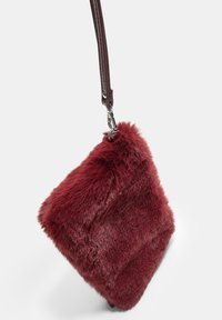 Burgundska umetna krzna torbica kvadratne oblike, s kratko usnjeno naramnico in srebrnim okovjem. Mehak tekstura z nekoliko sijočo površino.