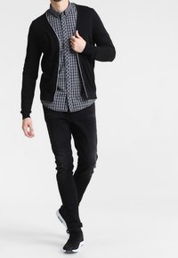 Czarny kardigan na niebiesko-białej koszuli w kratę, do tego czarne dżinsy i czarne trampki. Gładki materiał, dopasowany krój, nowoczesny styl.