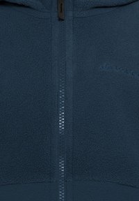 Giacca in pile di colore blu scuro con zip a tutta lunghezza, superficie testurizzata e dettagli con logo. Presenta un cappuccio aderente e una robusta zip.