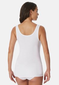 White cotton tank top with a scoop back design. Smooth texture and fitted shape, extending to hips, paired with low-rise white underwear.