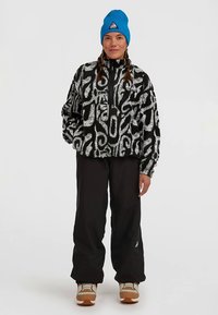 Fleece pullover in black and white abstract pattern with zip neck, complemented by a blue knit beanie and black pants. Brown and beige shoes.