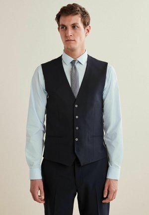 Marineblå vest med skræddersyet pasform, der har fem knapper, sidelommer, og en kontrasterende lyseblå skjorte samt et mønstret slips.