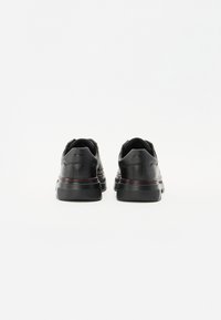 Baskets noires en cuir avec une texture lisse, dotées d'une épaisse semelle en caoutchouc et de accents de couture rouges autour de la semelle intermédiaire.