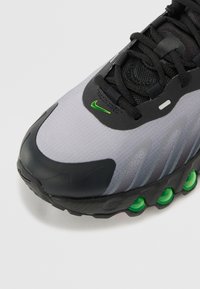 Baskets Nike avec une tige en maille grise, des accents noirs et des détails de semelle extérieure verts. Bout arrondi et semelle en caoutchouc texturé pour une meilleure adhérence.