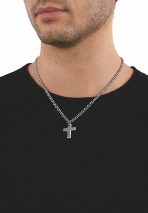 Brodaty mężczyzna noszący srebrny łańcuszek z wypolerowanym krzyżem na czarnej koszuli na białym tle.