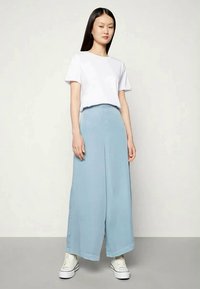 Calças largas de cor azul claro com uma textura suave, combinadas com uma t-shirt branca lisa de manga curta e ténis brancos.